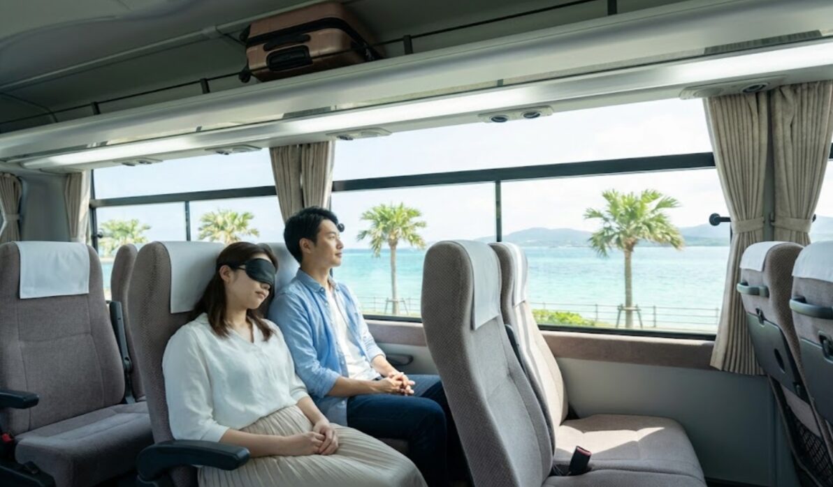 沖縄の高速バスの窓側の席で、運転の心配なくリラックスして南部の那覇へ向かう日本人旅行者（乗り捨て後の帰路のイメージ）。