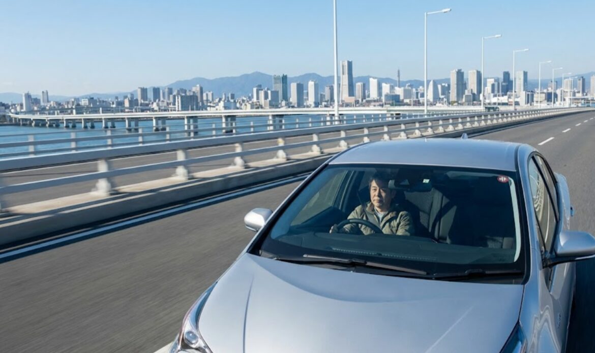 遠くの都市へと続く高速道路の橋を走行するレンタカー。長距離の乗り捨てを低価格で実現する「片道GO!」の利便性を表す。