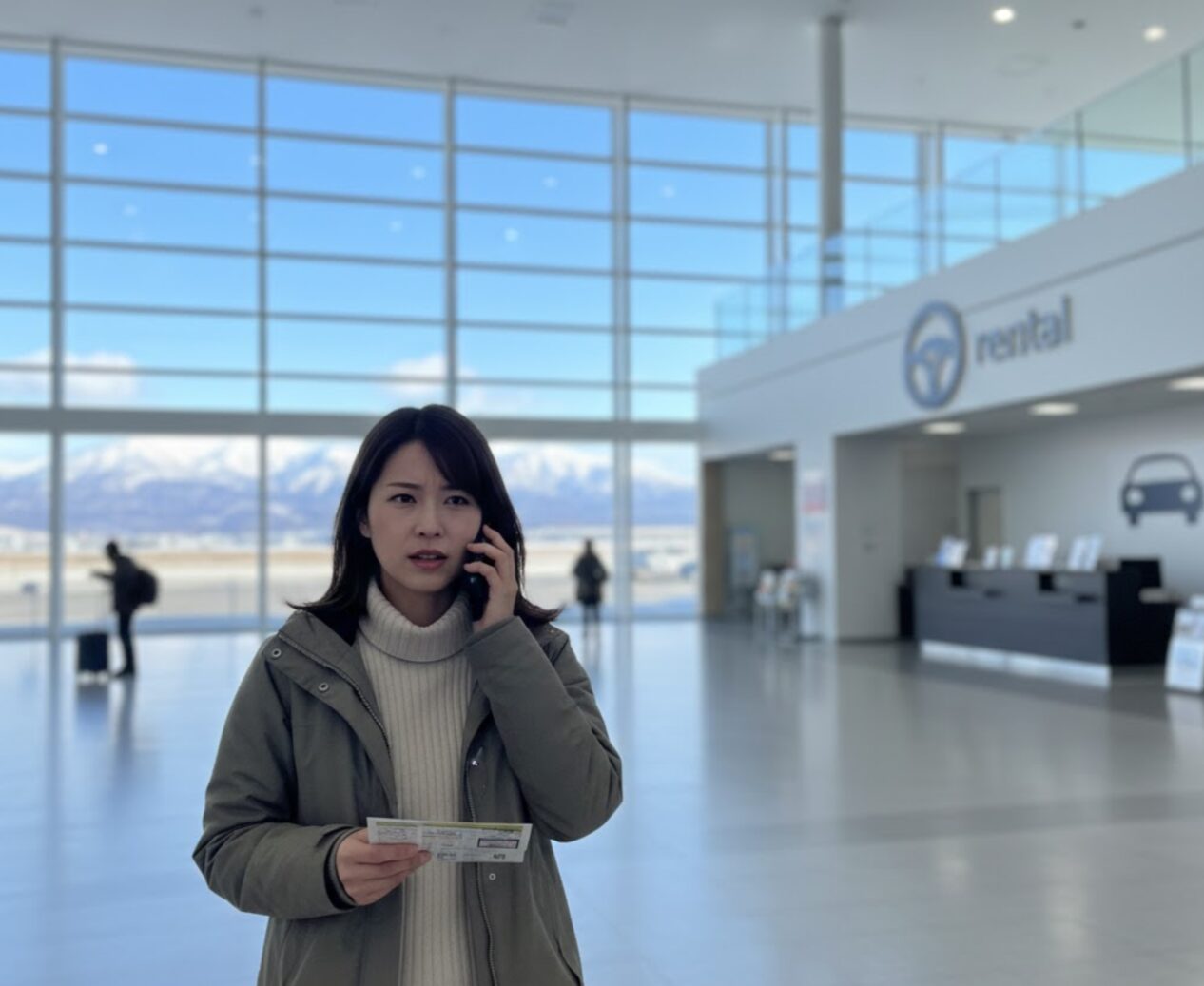 新千歳空港のロビーで、レンタカーの乗り捨て可否について店舗に電話で確認する日本の旅行者。