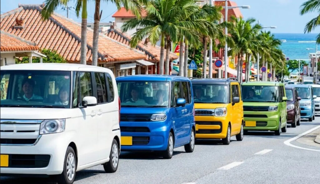 沖縄の青空の下、生活に必須なワゴンRやN-BOXなどの軽自動車が複数台並んで走行する様子。